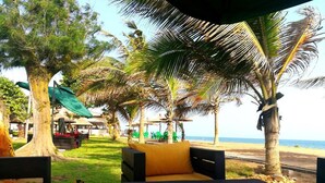 A beachside seating area with a table and chairs, surrounded by palm trees and a view of the sea. - Hotel Riviera Ramatou Plage (Lomé)