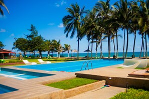 A pool area with lounge chairs, palm trees, and a view of the ocean.
