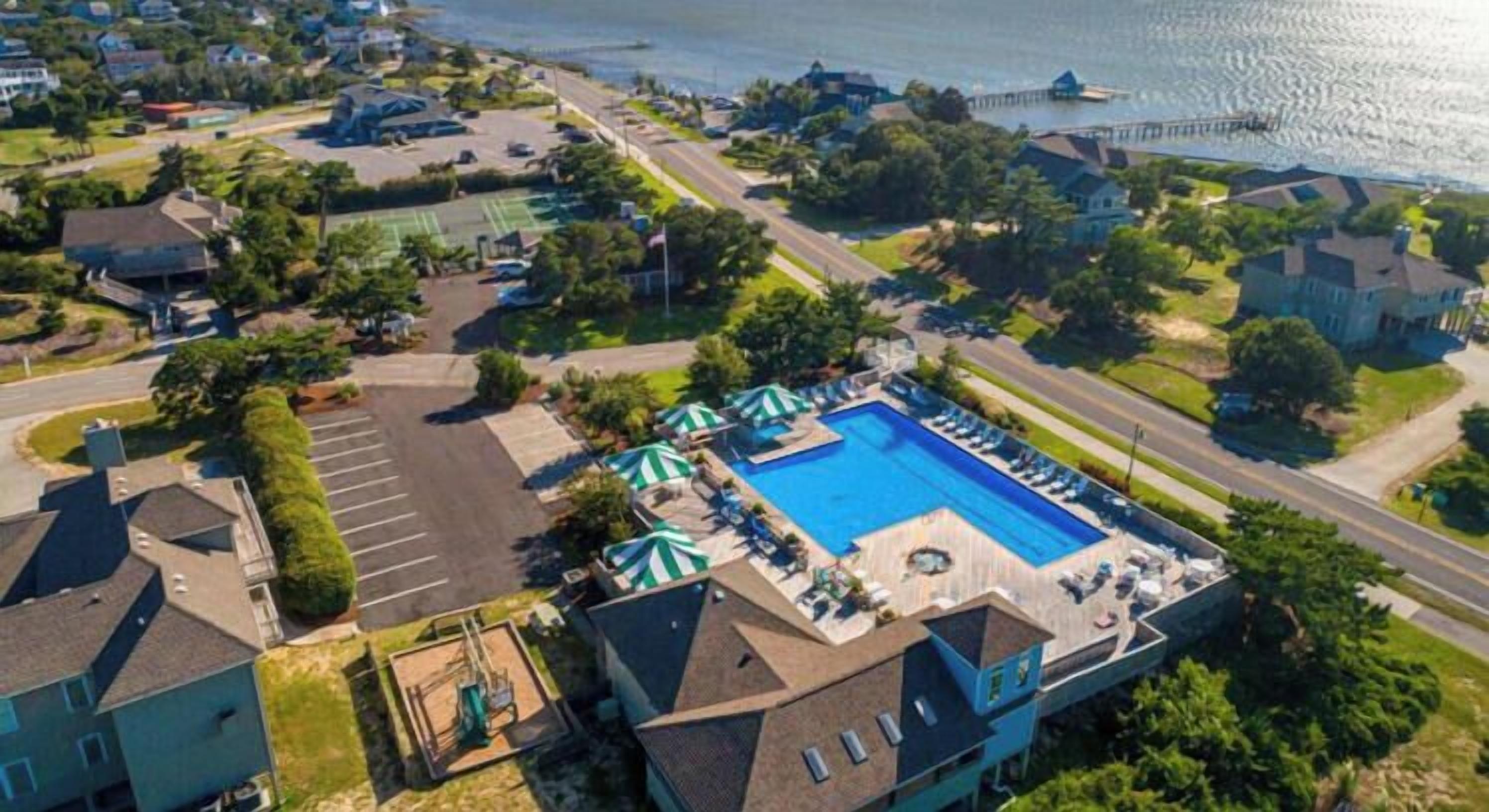 An aerial view of a residential area with a swimming pool, tennis courts, and a waterfront.