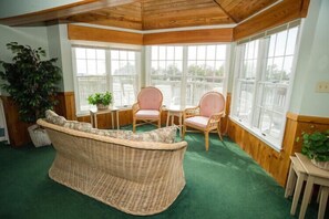 A corner room with a wicker sofa, two chairs, a small table, and large windows. - New Owner offering 20%rent discount for 7/28-8/4, 2028 Ramp Access-No Stairs (Duck)