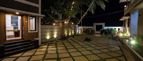 A well-lit courtyard with a checkered floor, a palm tree, and a building with a reception area.