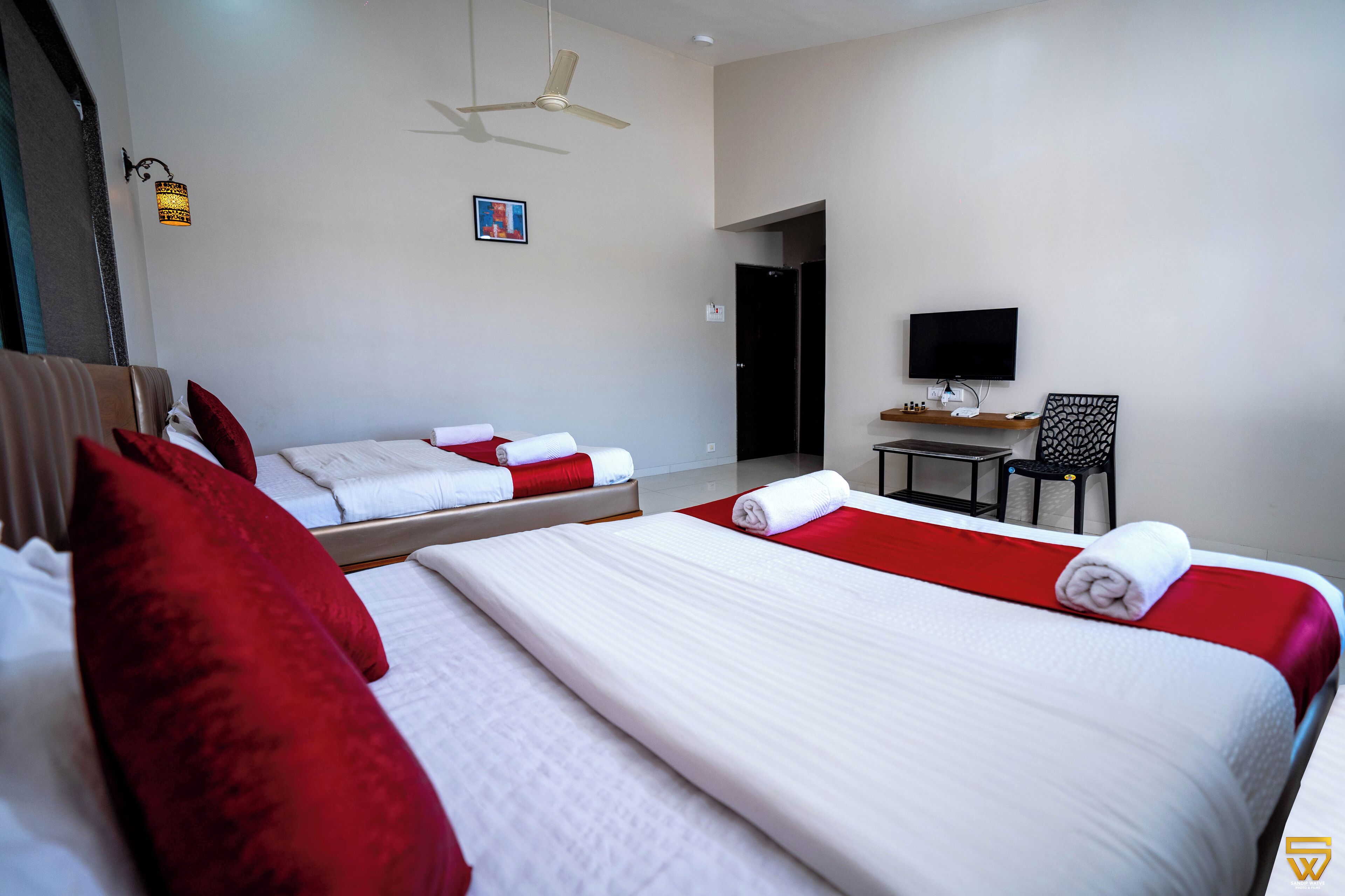 Een hotelkamer met twee bedden, een televisie, een plafondventilator en een bureau met stoel.