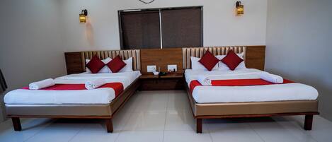 A hotel room with two beds, each with a wooden headboard, white bedding, and red accents. There is a window with a view, an air conditioning unit, and wall-mounted lights.