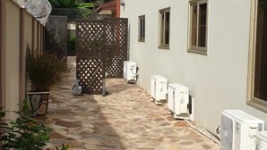 A courtyard with stone flooring, a wooden fence, and air conditioning units. - Janjay Hotel (Accra)