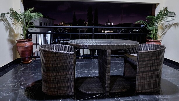 A round table with wicker chairs on a balcony with potted plants. - Janjay Hotel (Accra)