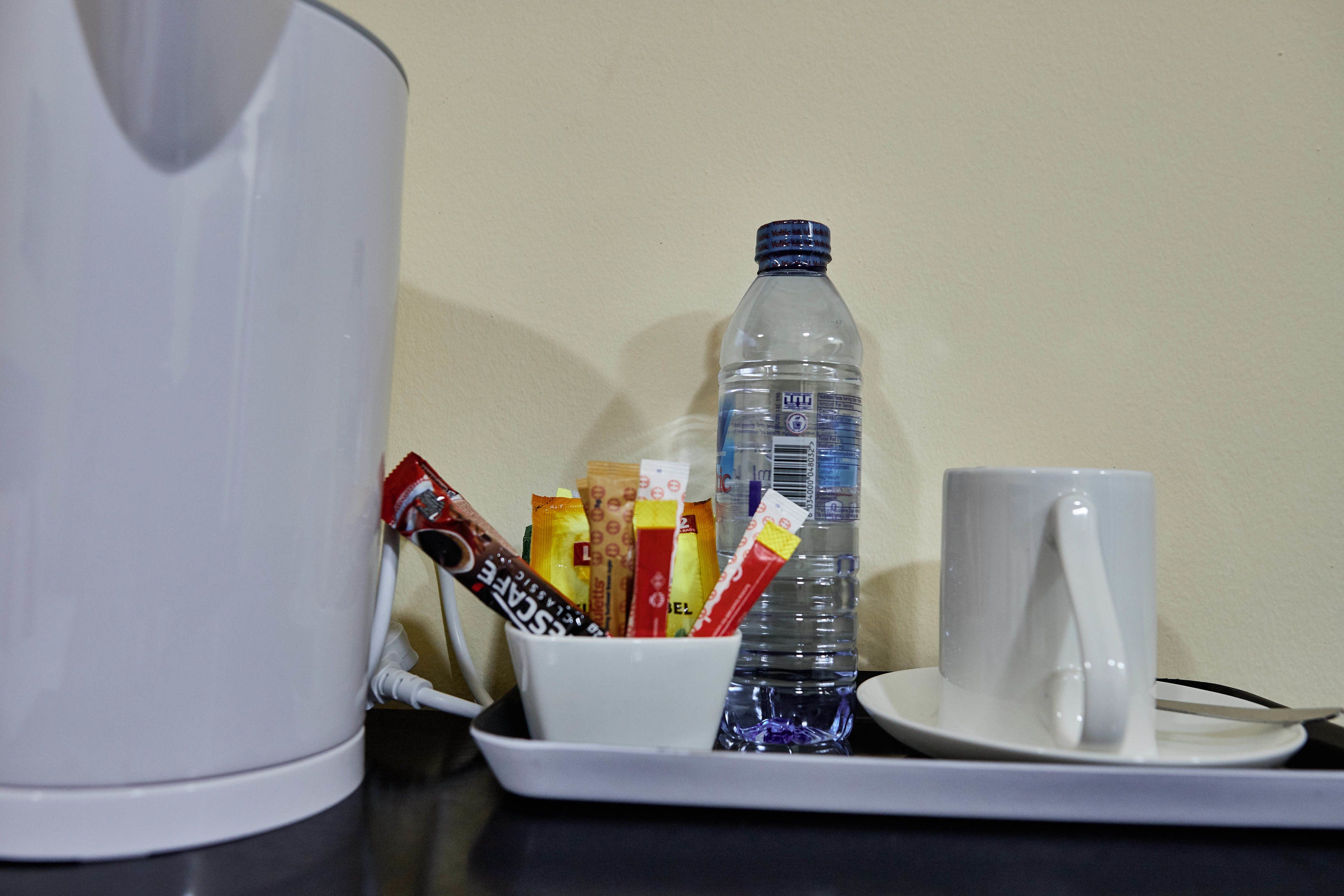 Una tetera blanca, una botella de agua, una taza y una bandeja con varios paquetes de snacks.