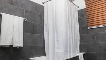A modern bathroom with a shower curtain, dark tiled walls, and a towel rack.