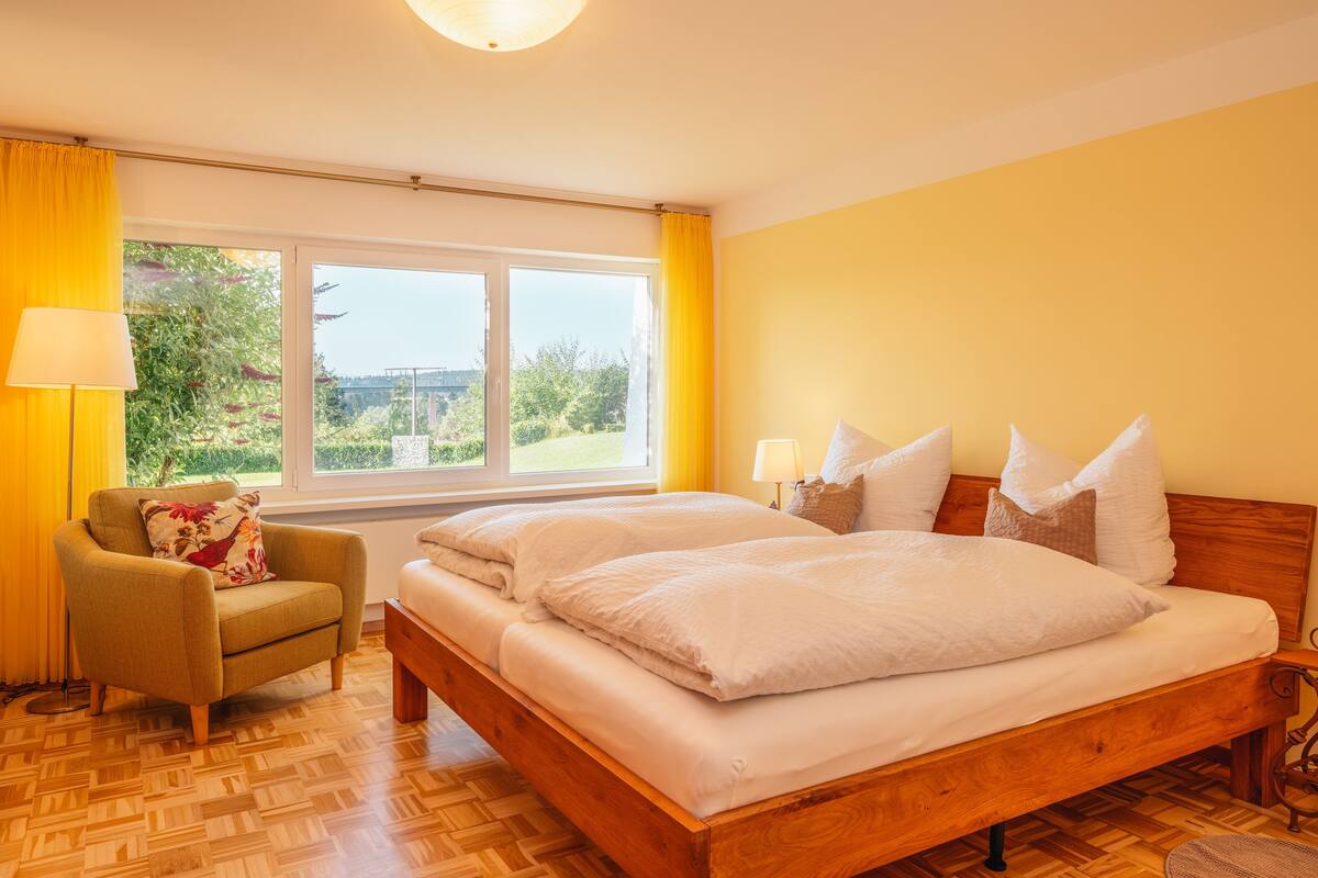 Ein Schlafzimmer mit einem hölzernen Bett, einem Stuhl und einem Fenster mit Vorhängen.