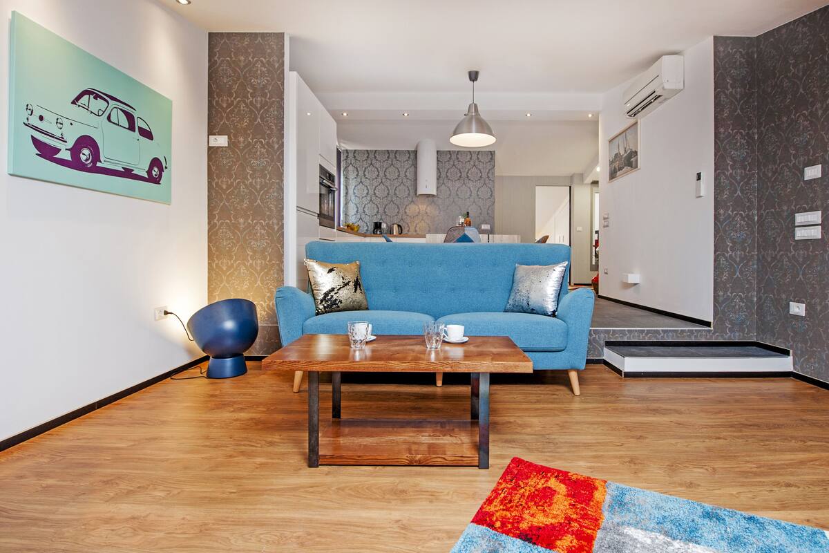 Una sala de estar moderna con un sofá azul, una mesa de centro de madera y una alfombra colorida.