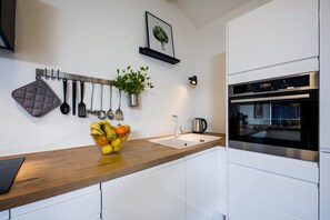 A modern kitchen with a wooden countertop, a sink, and a stainless steel oven. There are hanging utensils and a potted plant on the wall. - Lakovich Sea View Apartments (Rovinj)