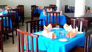A dining area with multiple tables covered in blue tablecloths, each set with white plates, silverware, and orange napkins. - Bykay Hotel (Sega)