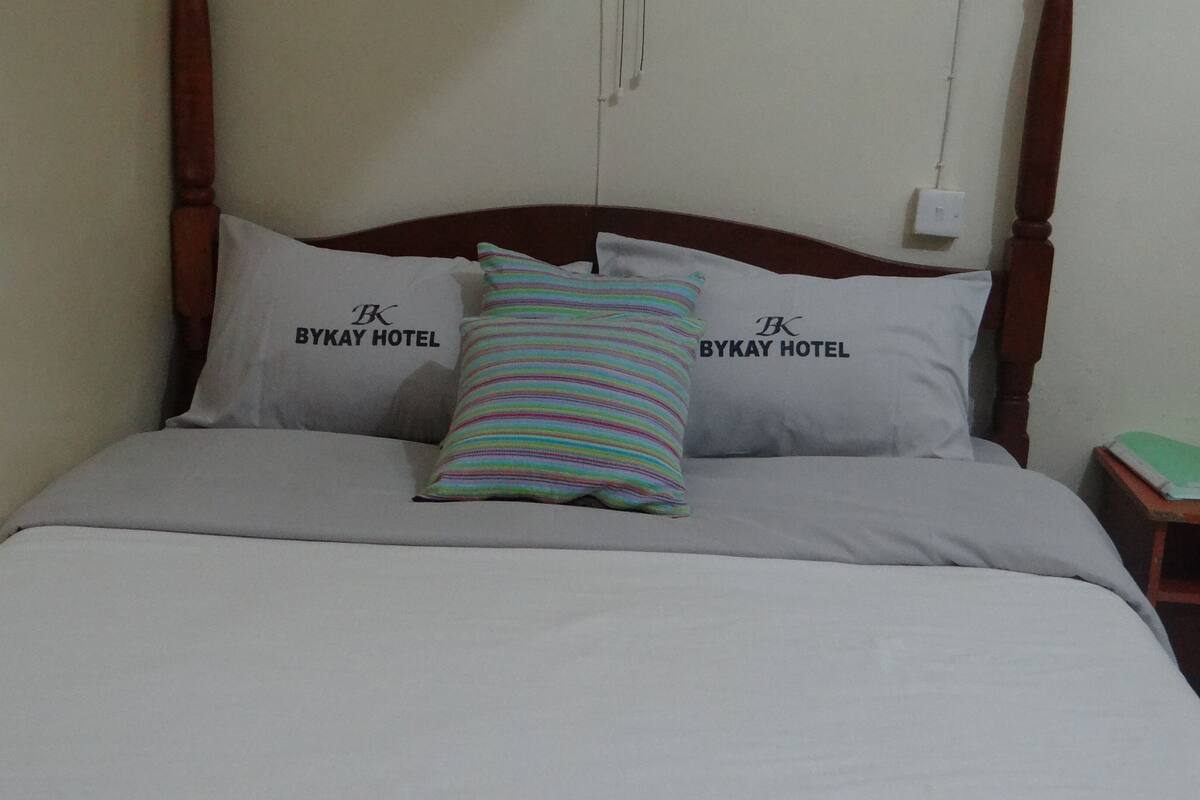 A bed with a grey bedspread and two pillows, one with a colorful striped pattern and the other with text.