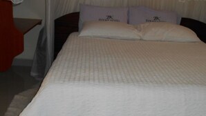 A hotel room with a bed, two pillows with a logo, a bedside table, and a red chair. - Bykay Hotel (Sega)