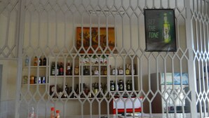 A bar area with shelves of various liquor bottles, a poster with the text "SET THE TONE", and a white metal partition. - Bykay Hotel (Sega)