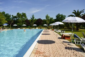 A swimming pool with lounge chairs and umbrellas, surrounded by trees and a brick pathway.