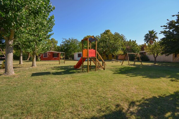 A playground with a slide and swings, surrounded by trees and buildings.