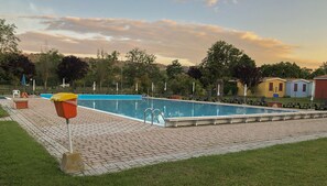 A rectangular swimming pool with a tiled deck, surrounded by lounge chairs and umbrellas. - Garden River - Campsite (Altidona)