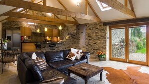 A spacious living area with a leather sofa, a wooden coffee table, and a stone wall backdrop. - Coriander Cottages (Fowey)