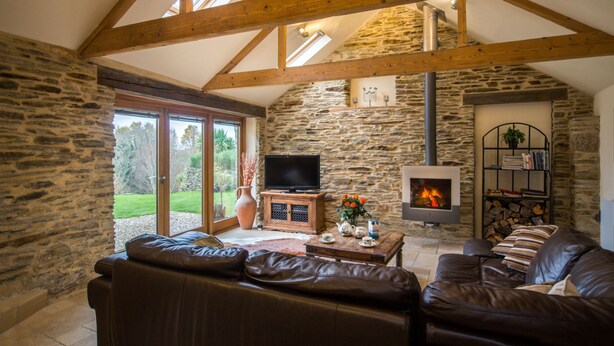 A cozy living room with stone walls, a fireplace, a television, and leather sofas. - Coriander Cottages (Fowey)