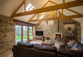 Un salón acogedor con paredes de piedra, chimenea, televisor y sofás de cuero.