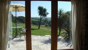 A room with a large sliding glass door leading to an outdoor patio area with a table and umbrella. - Coriander Cottages (Fowey)