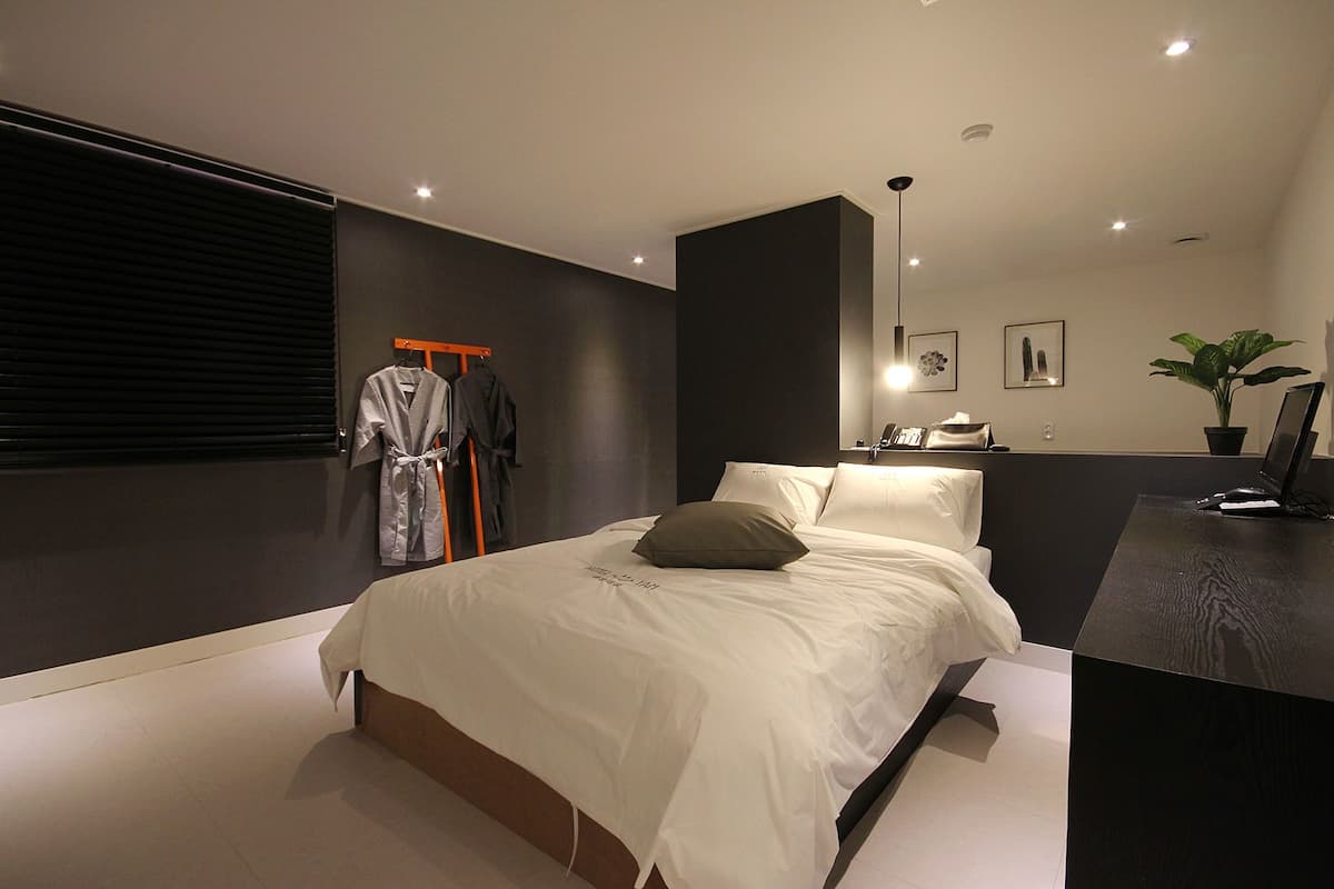 Un dormitorio moderno con una cama grande, una mesita de noche, un escritorio, una silla, un perchero para bata y una planta en maceta.