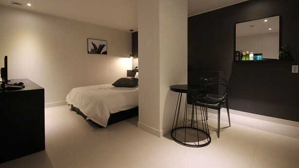 A modern bedroom with a bed, bedside table, lamp, and a chair. - Busan Haeundae Hotel A (Busan)