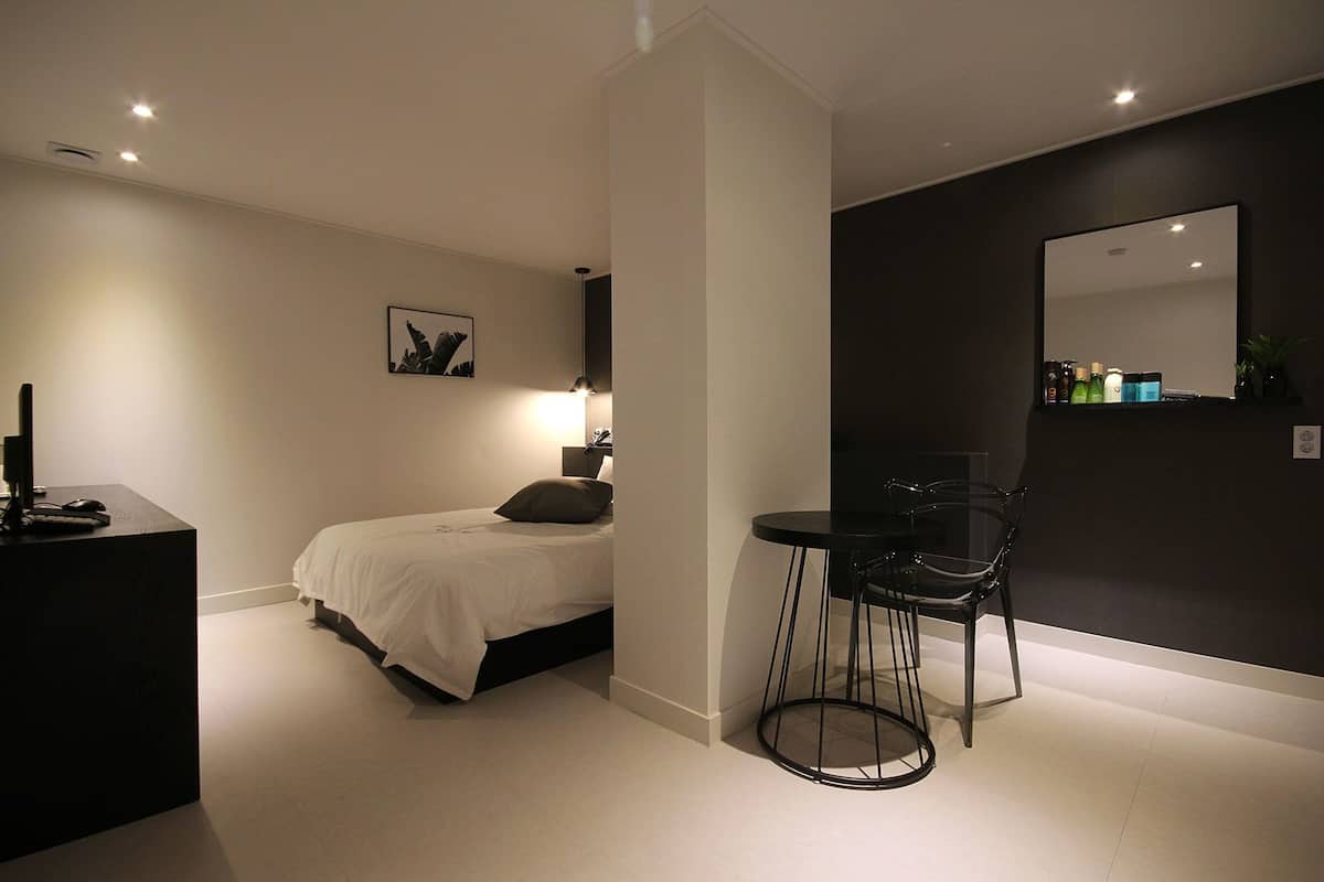 Un dormitorio moderno con cama, mesita de noche, lámpara y una silla.