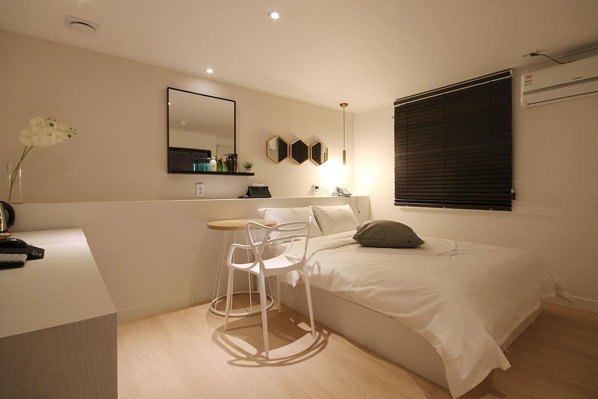 Un dormitorio con cama, escritorio, silla, espejo y ventana con persianas.