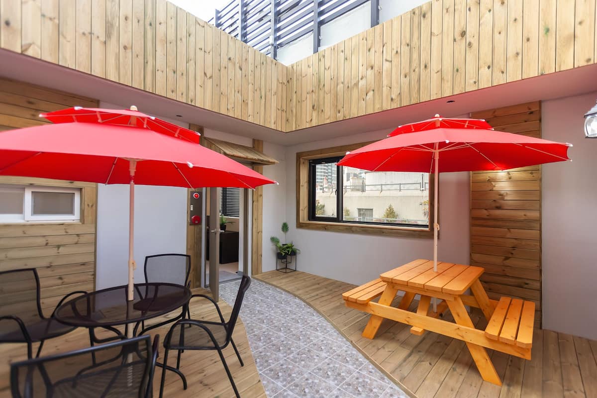 Un interior de madera con una mesa redonda y sillas, dos sombrillas rojas y un banco de madera.