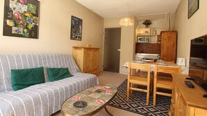 A compact living space with a striped sofa, a small dining table, a coffee table, a kitchen area with a microwave, and a TV.