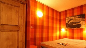 A room with a wooden bed, a red chair, and a checkered wall.