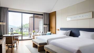 A modern hotel room with two beds, a desk, and a balcony with a view.
