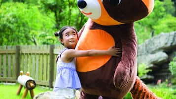 Children can play and interact with our friendly raccoon mascot in a lush outdoor setting.