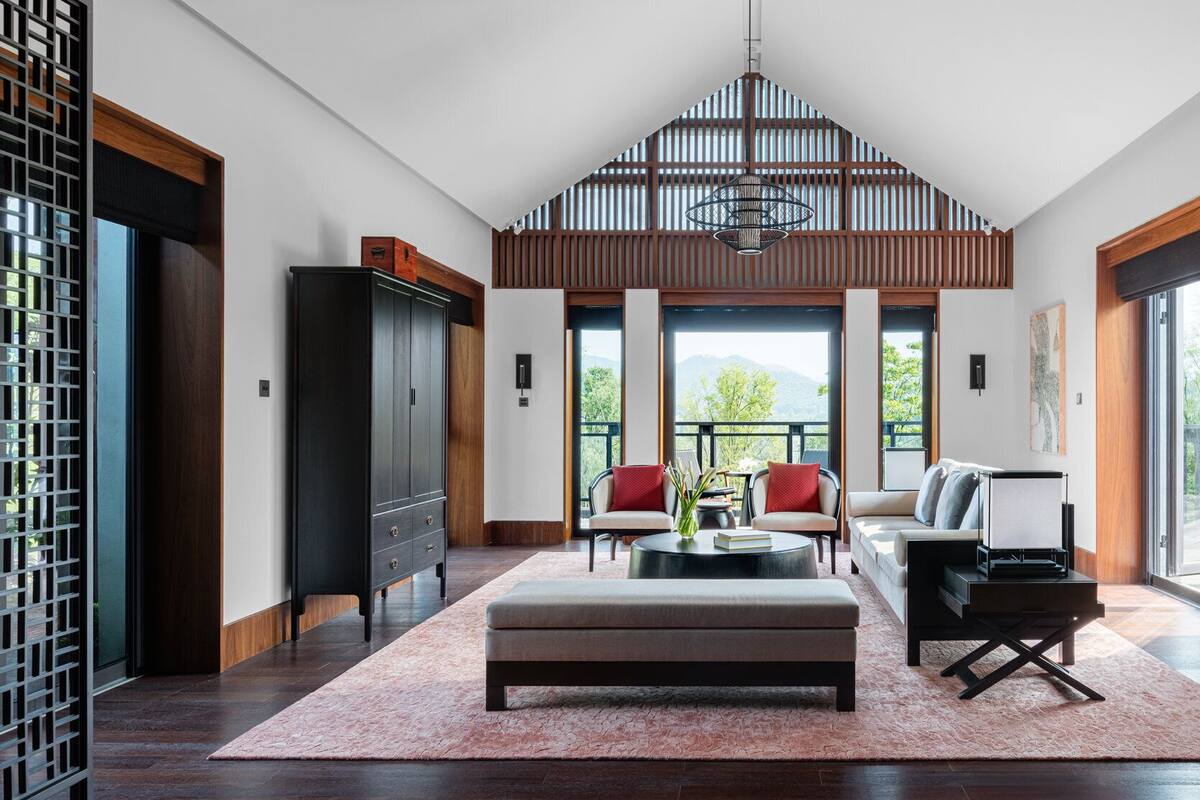 A spacious living area with a high ceiling, a large window offering a view of the outdoors, a central seating arrangement, and a modern chandelier.