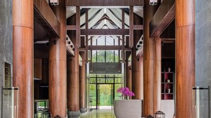 A spacious lobby with high wooden columns, a central planter with flowers, and a view of the outdoors.
