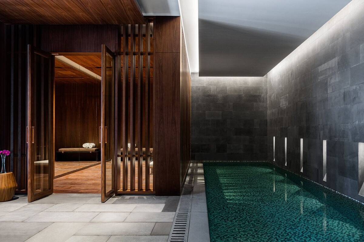 A modern indoor pool area with a wooden partition, a bench, and a tiled floor.