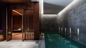 A modern indoor pool area with a wooden partition, a bench, and a tiled floor.