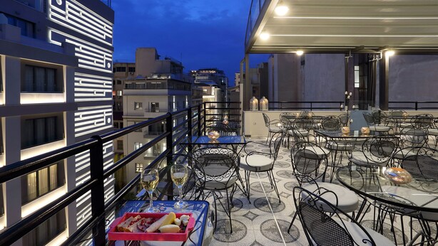 An outdoor terrace with tables and chairs, a buffet table with food, and a modern building in the background. - V1935 Luxurious Apartments (Athens)