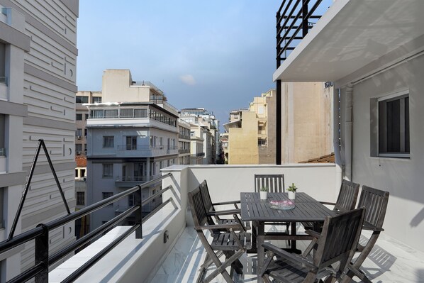 A rooftop terrace with a table and chairs, a potted plant, and a view of surrounding buildings.