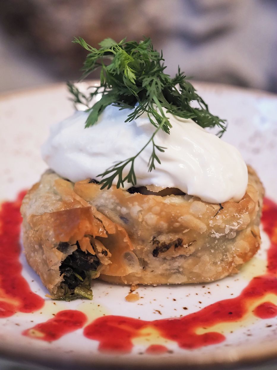 A dish with a creamy topping and a garnish of green herbs.