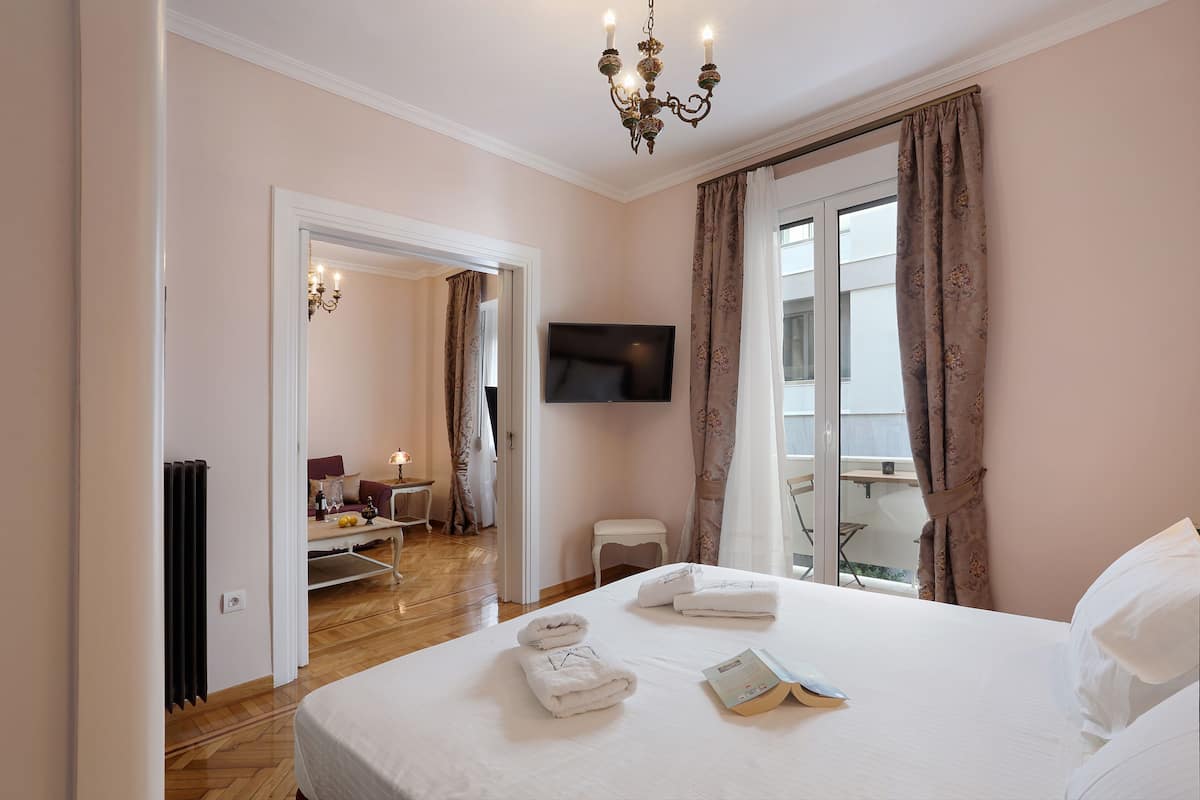 A hotel room with a large bed, a flat-screen TV mounted on the wall, and a balcony with a view.
