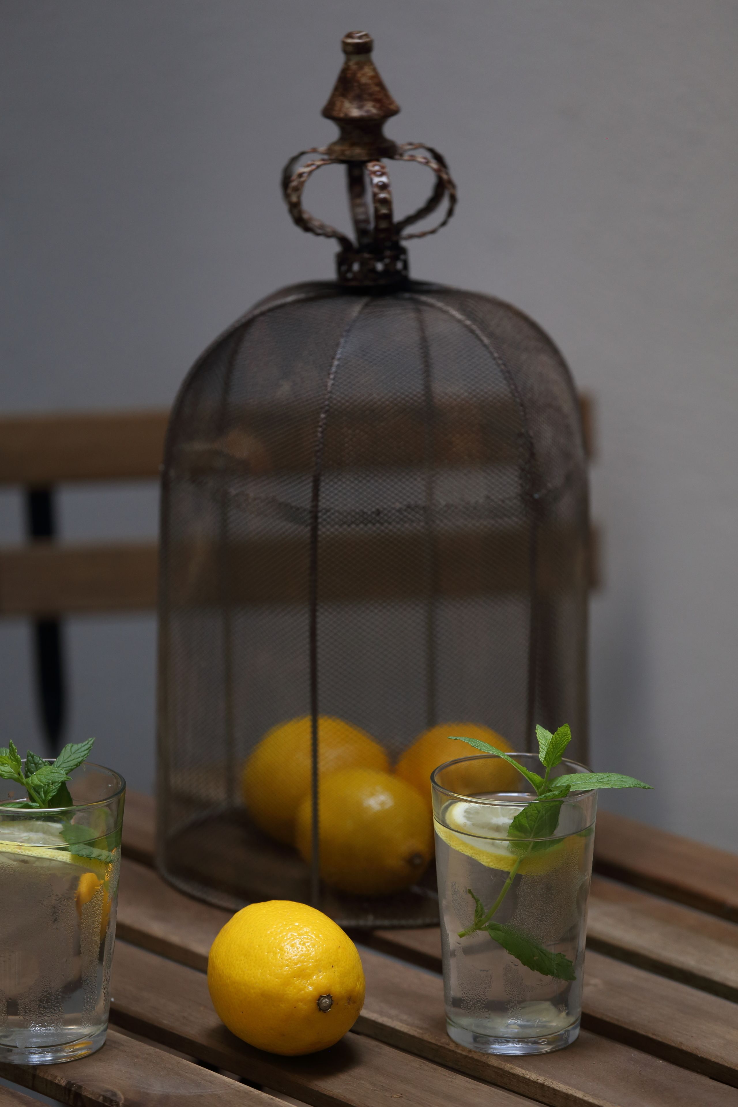 A glass of water with a lemon slice and mint leaves on a wooden table.