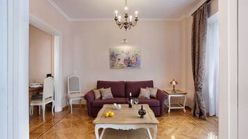 A living room with a sofa, a coffee table, a chandelier, and a painting on the wall.