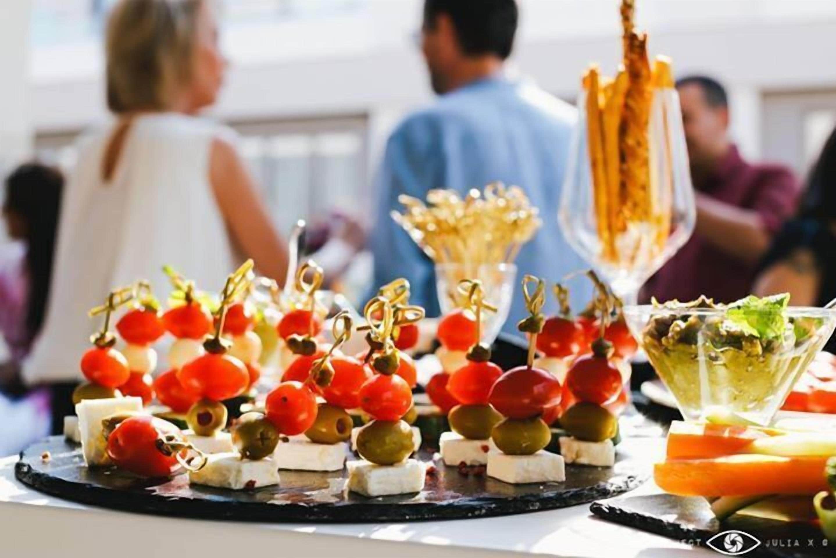 A buffet table with various food items including cheese, olives, cherry tomatoes, and a salad in a glass bowl.