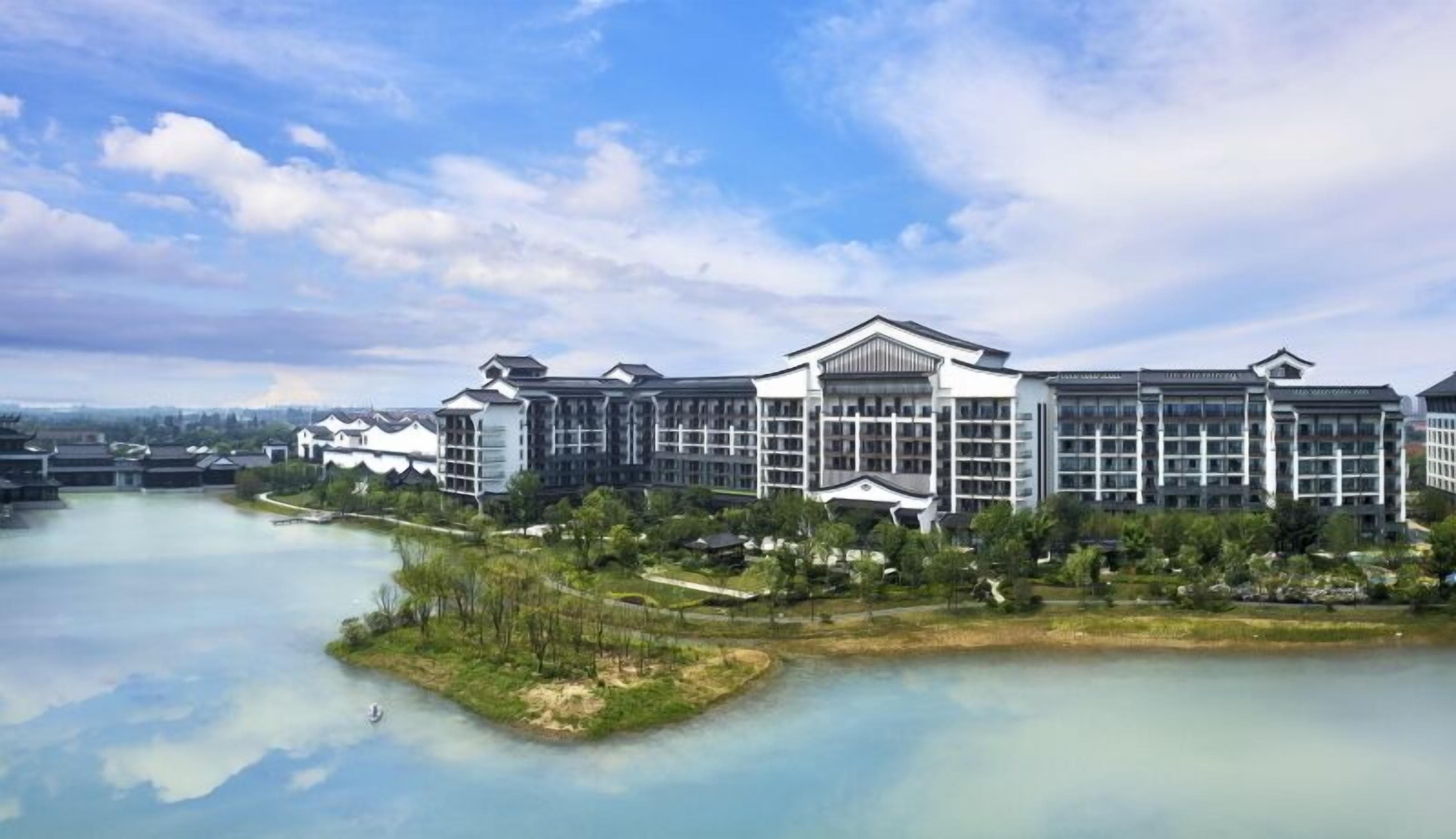 A large hotel with multiple buildings, a body of water, and surrounding greenery.