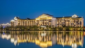 Un hôtel à plusieurs étages, doté d’une façade symétrique, de grandes fenêtres et dont l’image se reflète dans l’eau devant l’établissement.