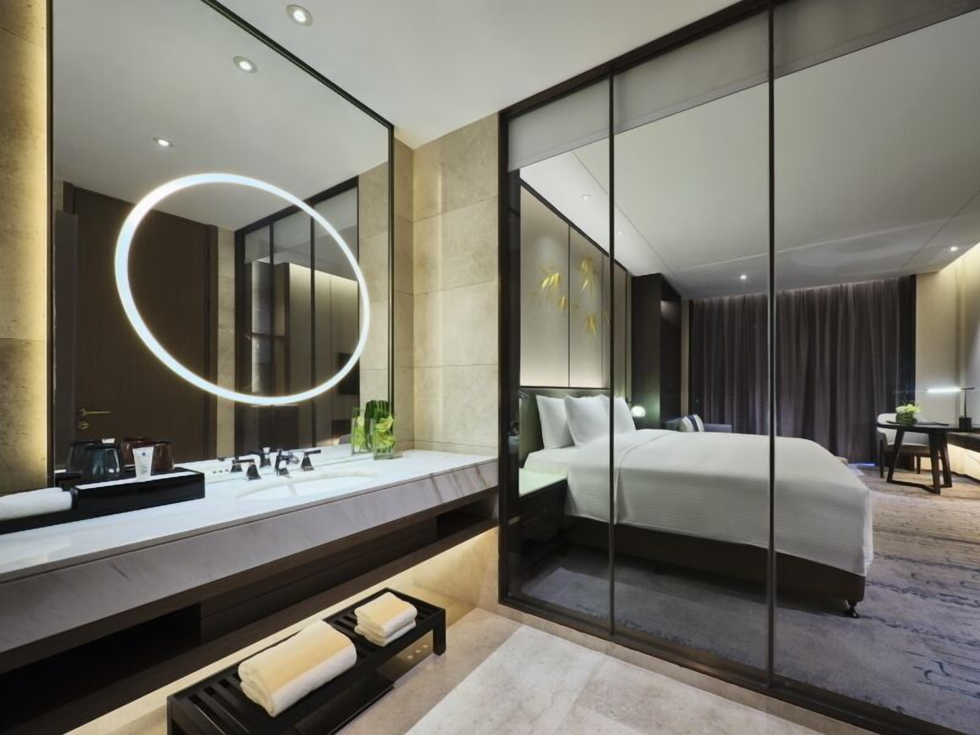 Une chambre d’hôtel moderne, dotée d’un grand miroir, d’un lit, d’un bureau et d’une salle de bain avec un lavabo et un miroir.