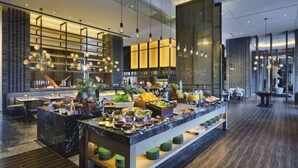 Un hall d’hôtel moderne doté d’un espace buffet central, d’un sol en marbre et de luminaires contemporains.