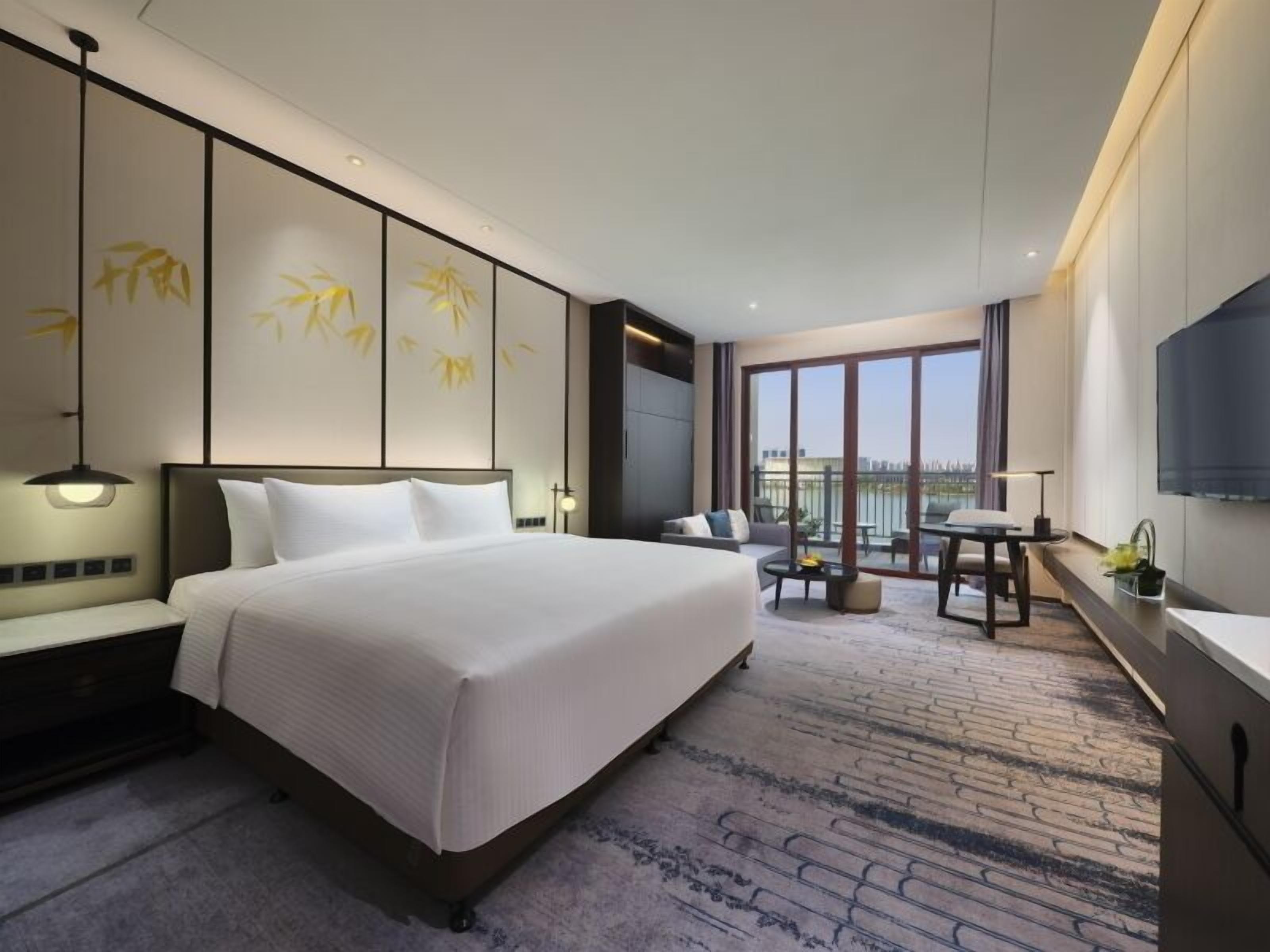 Ein Hotelzimmer mit einem großen Bett, einem Schreibtisch, einem Sessel und einem Fernseher.